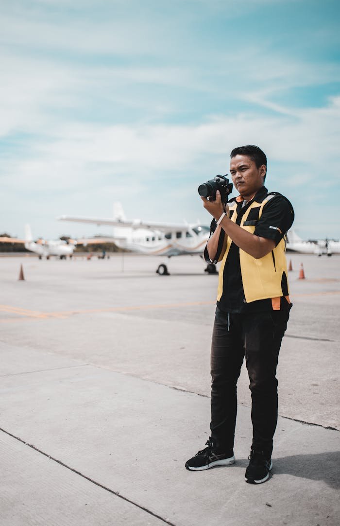 Man with camera photographing airplanes on an airport runway during the day.